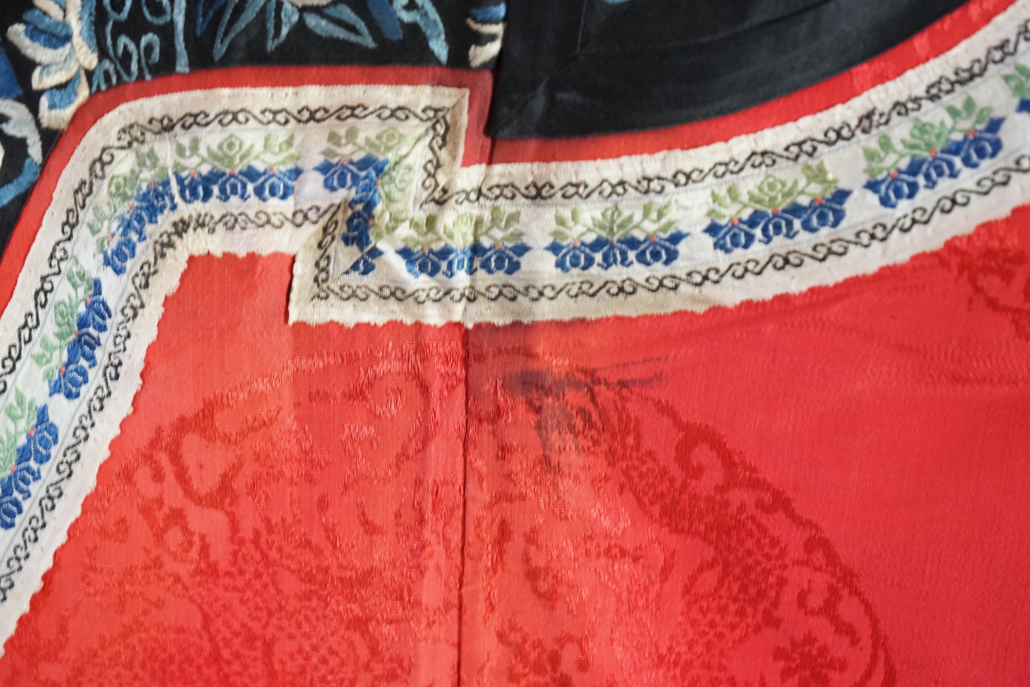 A late 19th century Chinese Manchu ladies red silk damask robe, with black and blue silk embroidered borders, ornately edged cream floral silk braiding, length from neck (back) to bottom edge 132cm long. Condition - stai